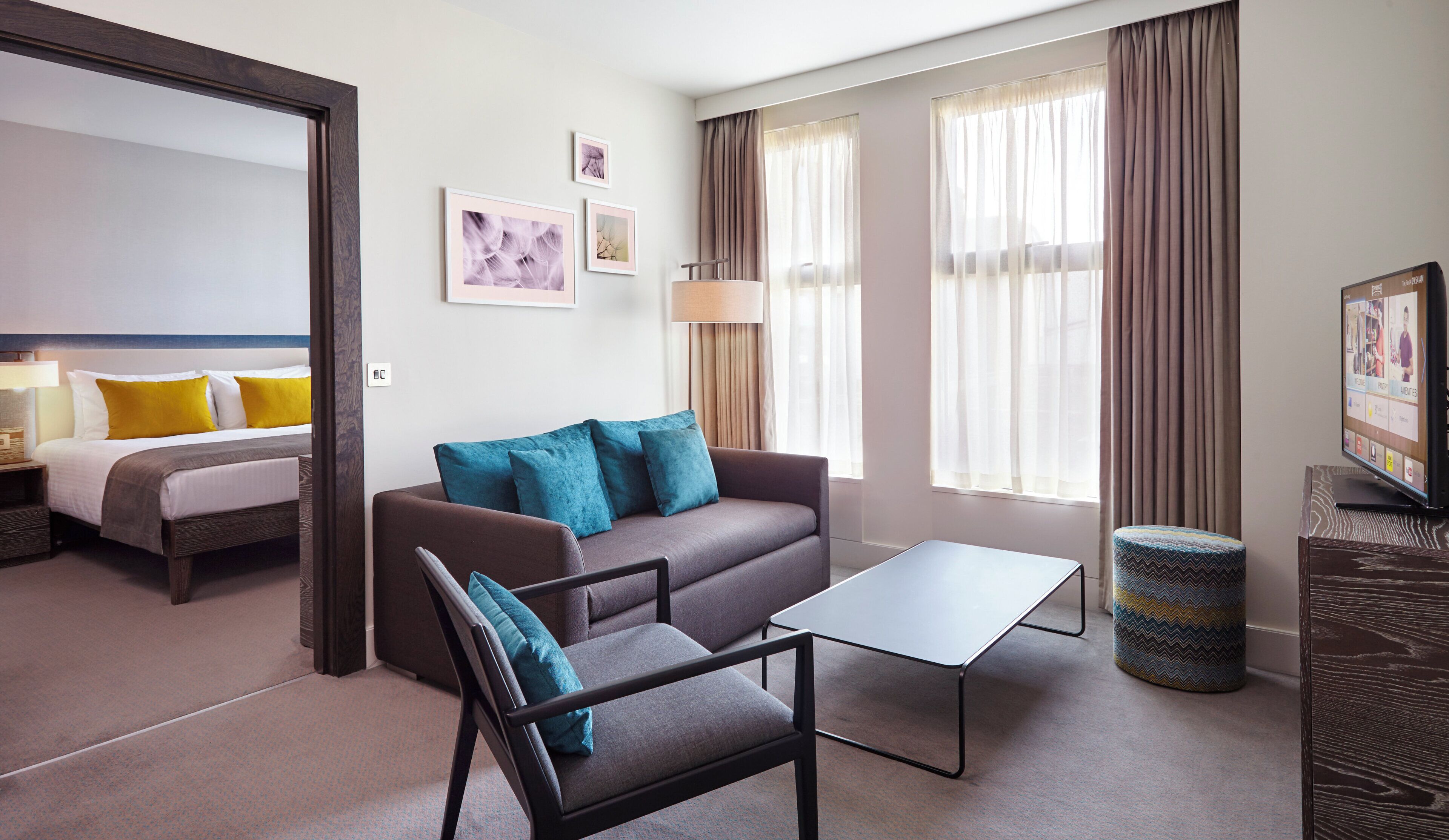 A hotel room with a bed, a sofa, a coffee table, a TV, and a window with curtains.