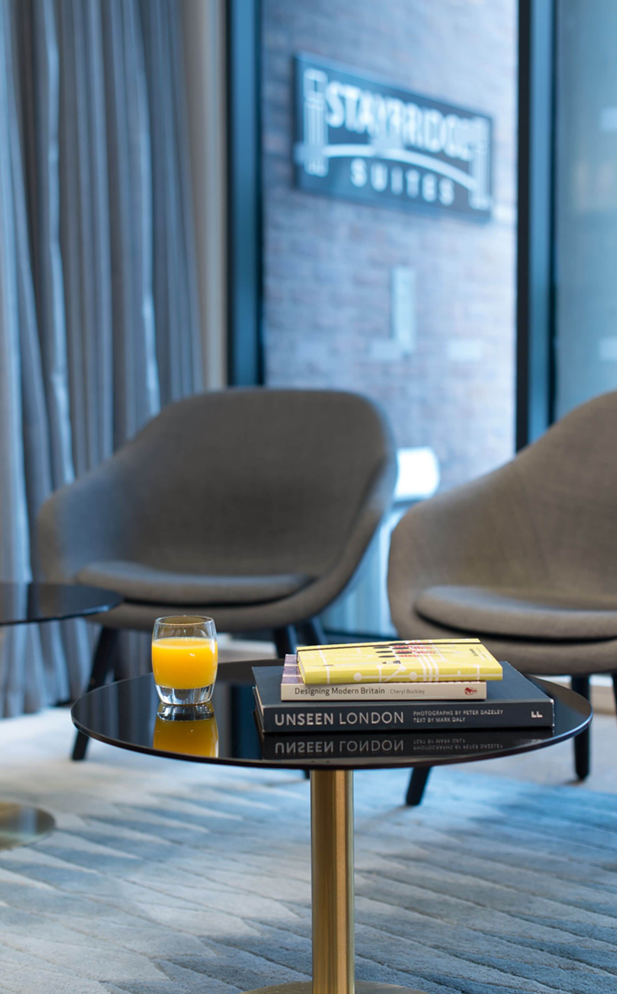 A modern hotel room with a glass table holding a glass of orange juice and a stack of books.