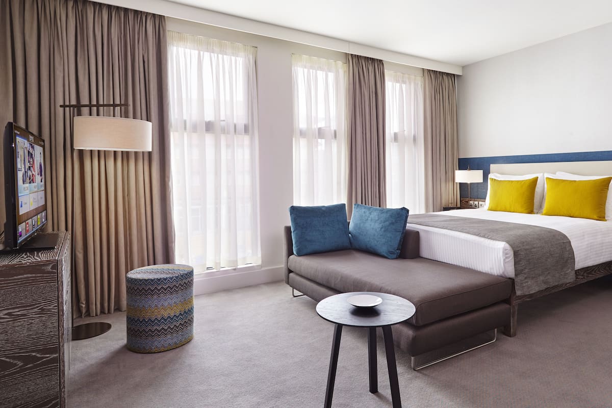 Ein Hotelzimmer mit einem Bett, Nachttischen, einem Sofa, einem kleinen runden Tisch und einem Fernseher auf einem Schrank.