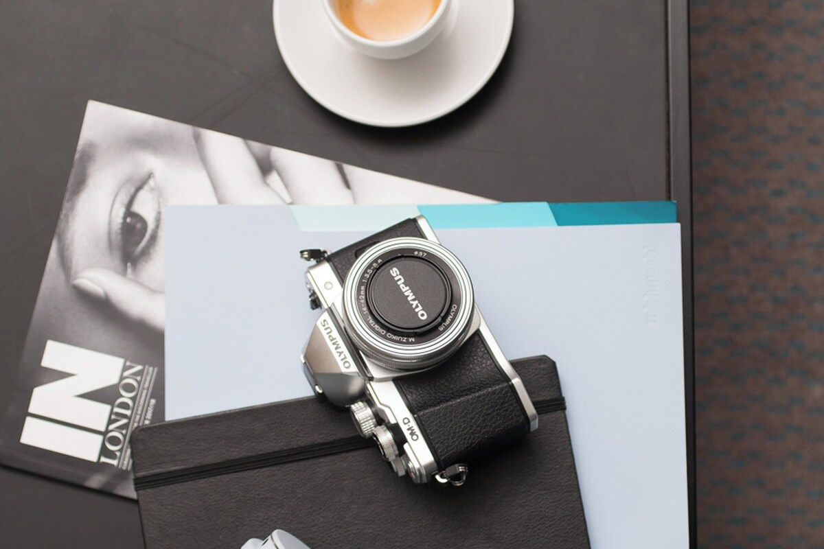 A vintage camera with a leather strap on a table, a magazine, and a cup of coffee.