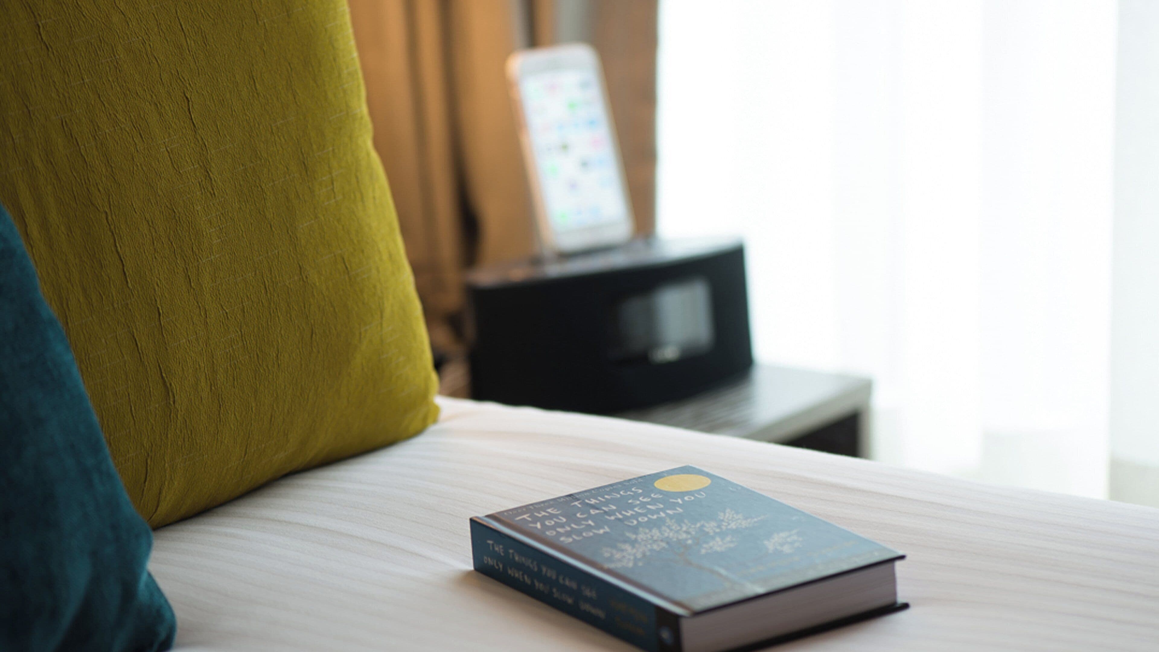A book titled 'The Things You Can See When You Slow Down' on a bed with a pillow and a television in the background.