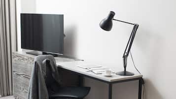 A modern workspace with a desk, chair, and a standing desk lamp. A flat-screen TV is mounted on the wall.