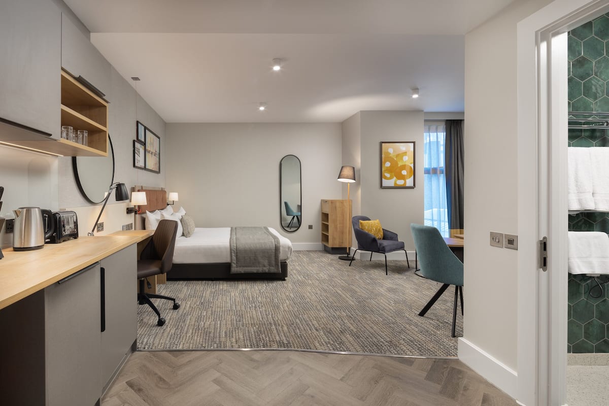 Ein modernes Hotelzimmer mit Bett, Schreibtisch, Stuhl und Blick ins Bad.