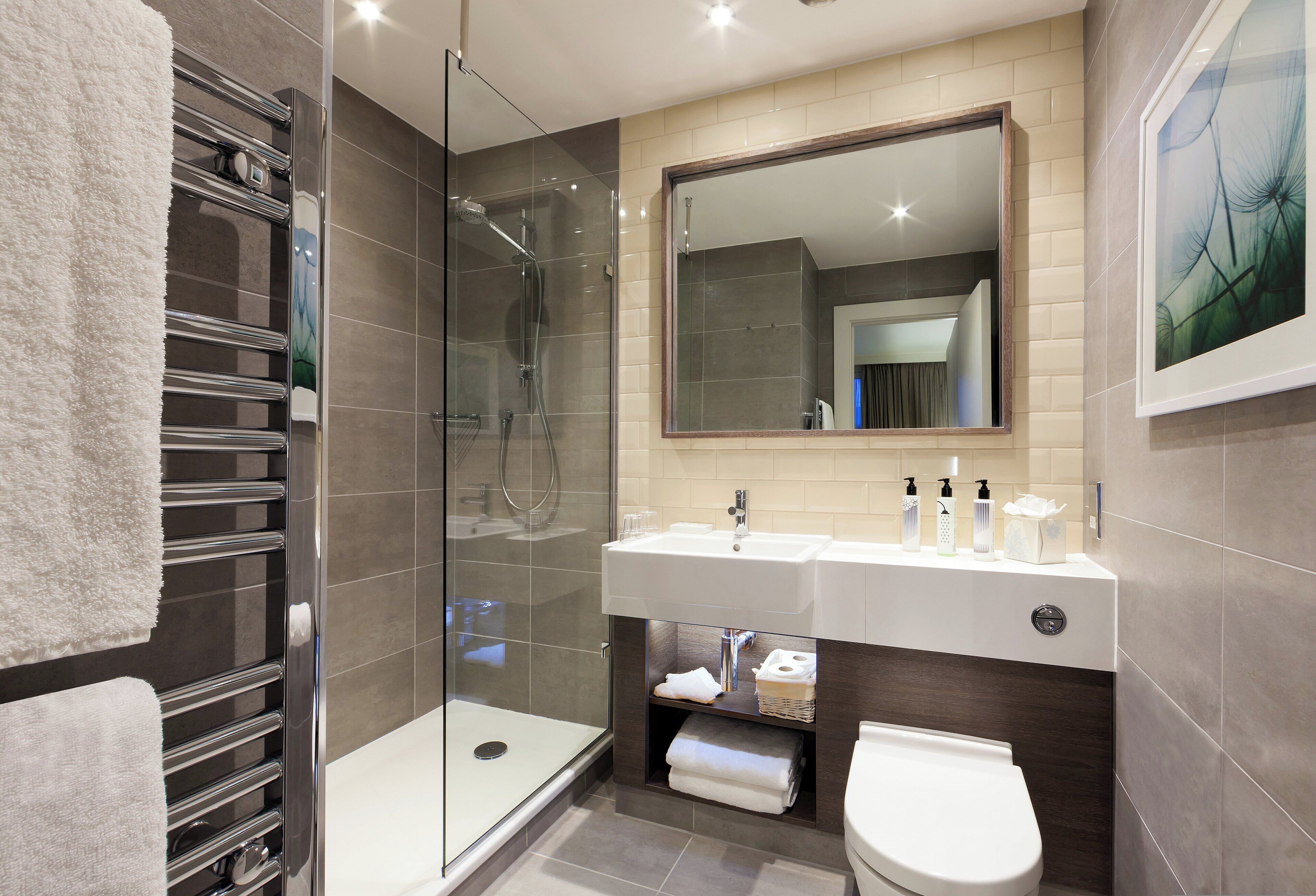A modern bathroom with a glass shower enclosure, a white sink with two faucets, and a toilet.