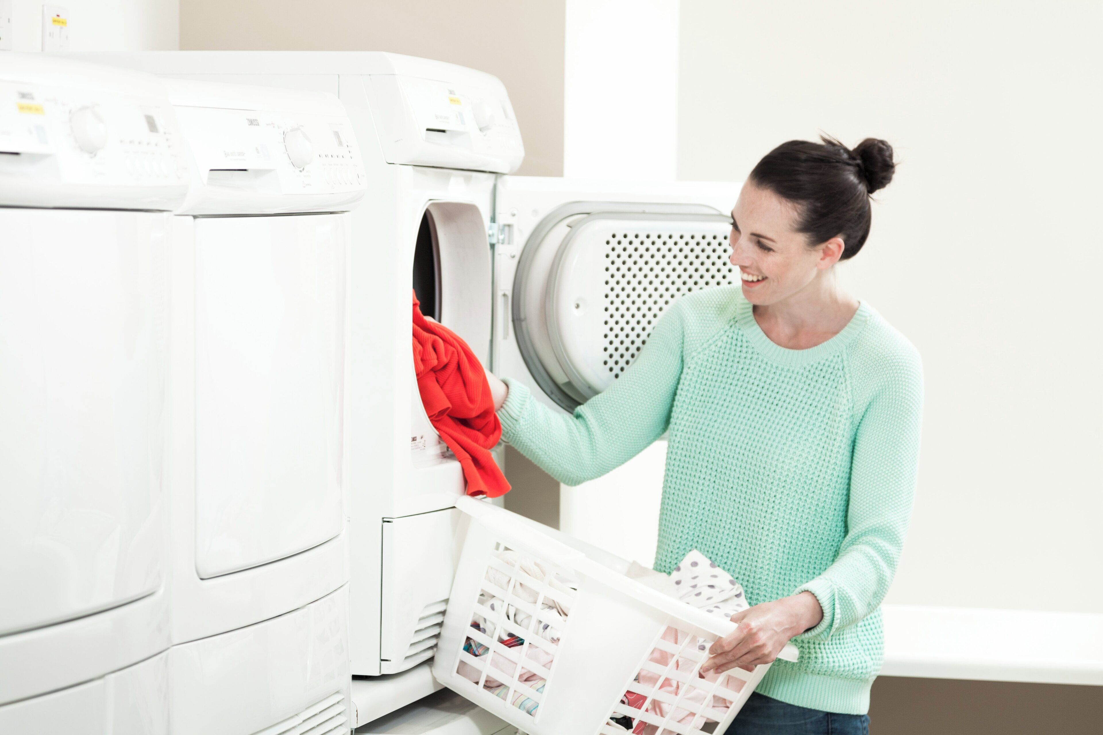 A person loading a white laundry basket into a front-loading washing machine.