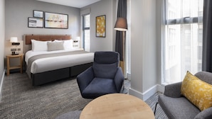 A hotel room with a large bed, a chair, a sofa, and a small table. There are framed pictures on the wall and a lamp next to the bed. - Staybridge Suites London - Vauxhall by IHG (London)