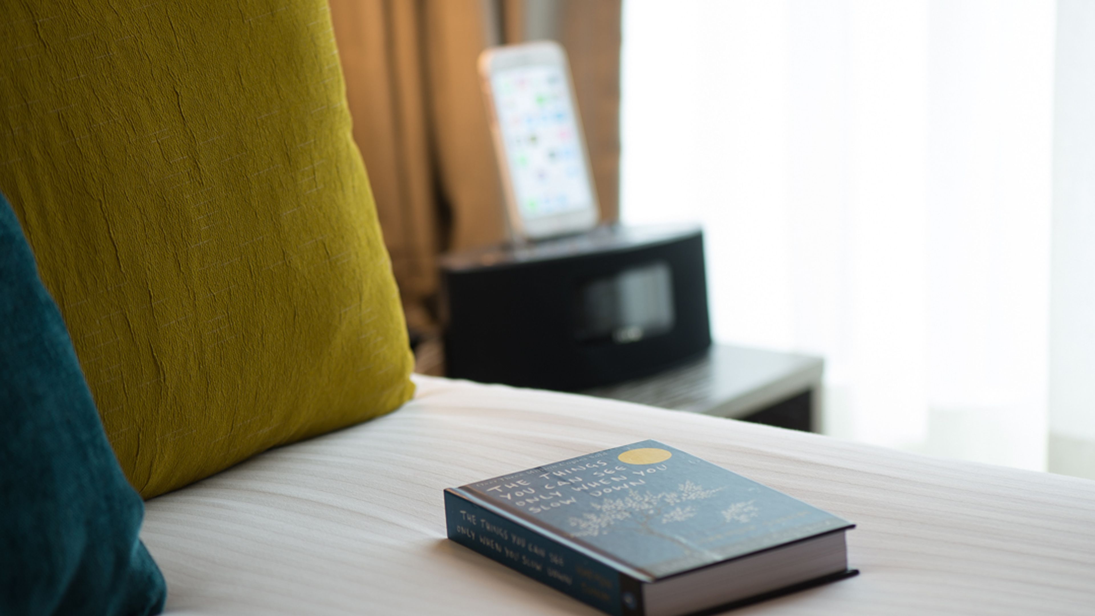 Un libro titulado "Las Cosas Que Ves Solo Cuando Tomaste tu Tiempo" sobre una cama con cabecera de madera y un cojín verde.