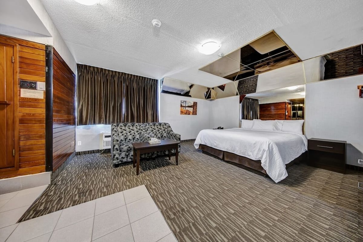 A hotel room with a bed, a sofa, a small table, and a mirror.