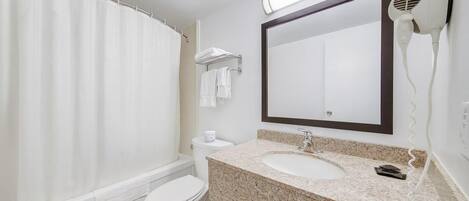 A bathroom with a shower curtain, toilet, sink, and a hairdryer mounted on the wall.