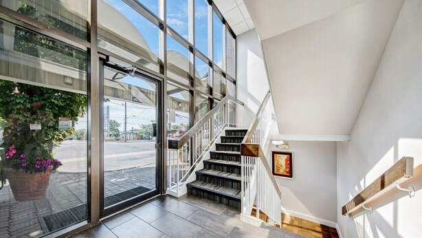 A modern interior with a staircase, large windows, and a potted plant. - Deluxe Inn (Toronto)