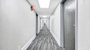 A long, narrow hotel corridor with a patterned carpet, white walls, and doors on both sides. - Deluxe Inn (Toronto)