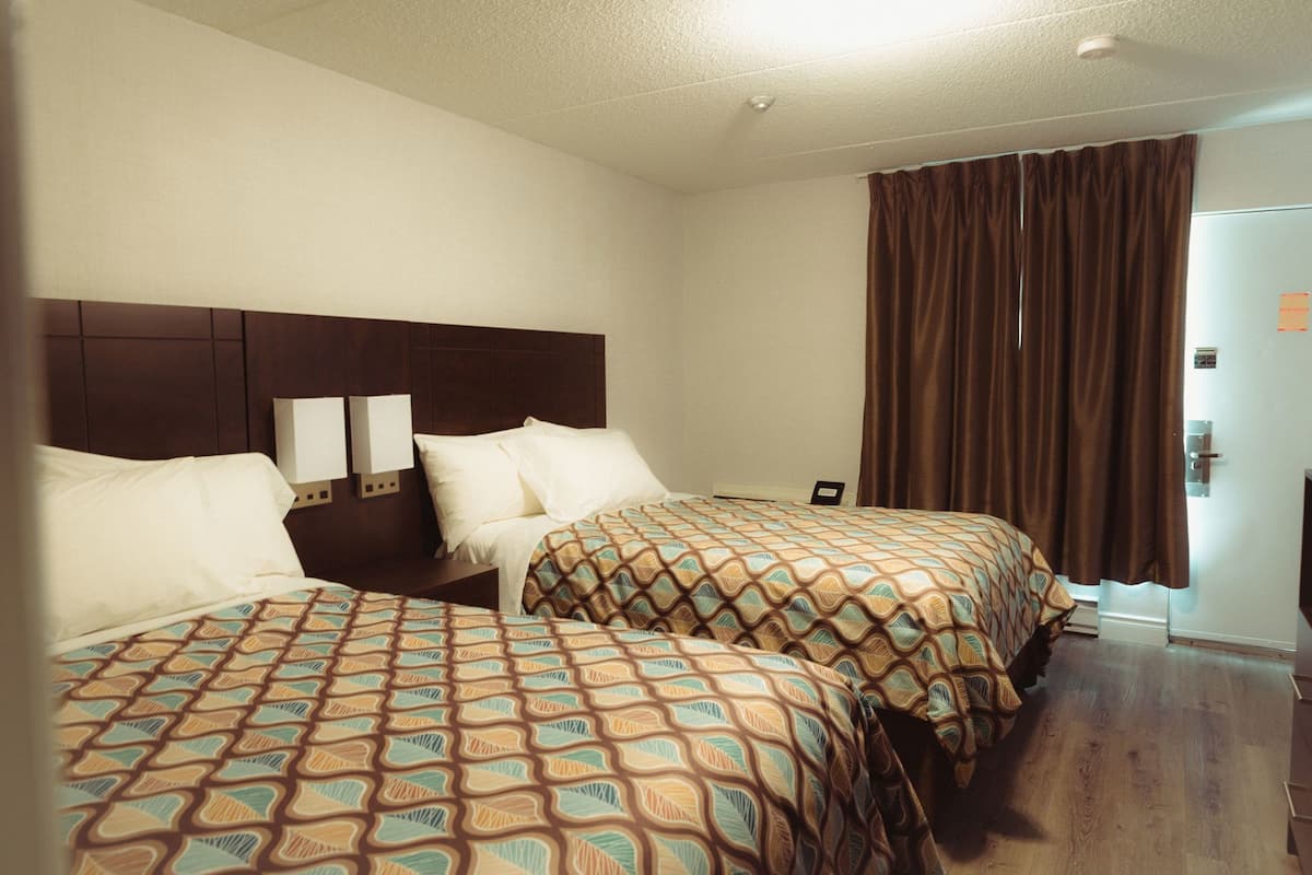 Habitación de hotel con dos camas, cabecera de madera, mesita de noche y una puerta con manija.