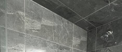 A modern shower with a glass door, a handheld showerhead, and a wall-mounted faucet.