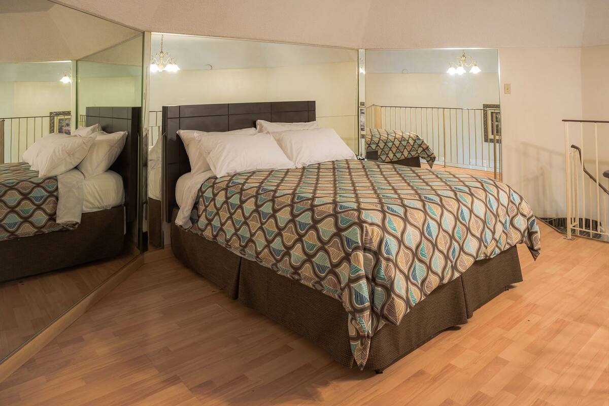 Un dormitorio con una cama grande, un espejo, una escalera y suelo de madera.