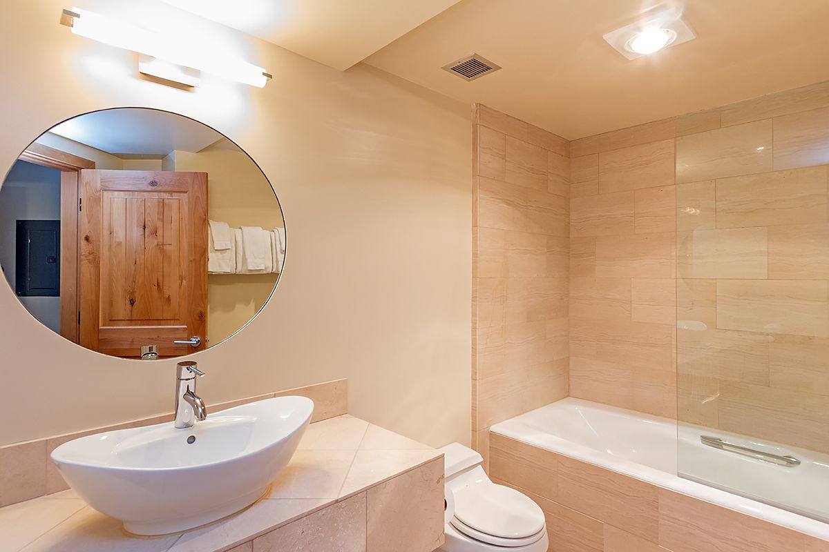 A modern bathroom with a round mirror, a white sink, a toilet, and a glass-enclosed shower.