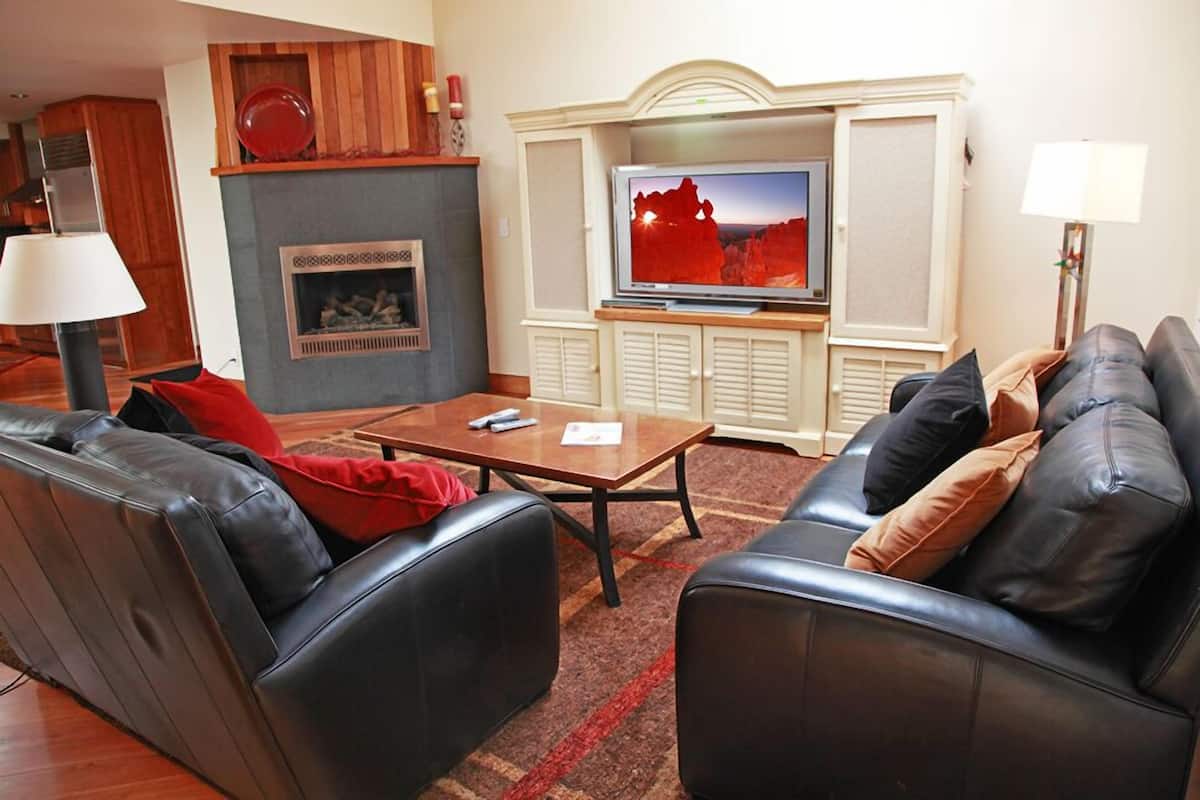Una sala de estar con chimenea, televisor, sofás de cuero y una mesa de centro.