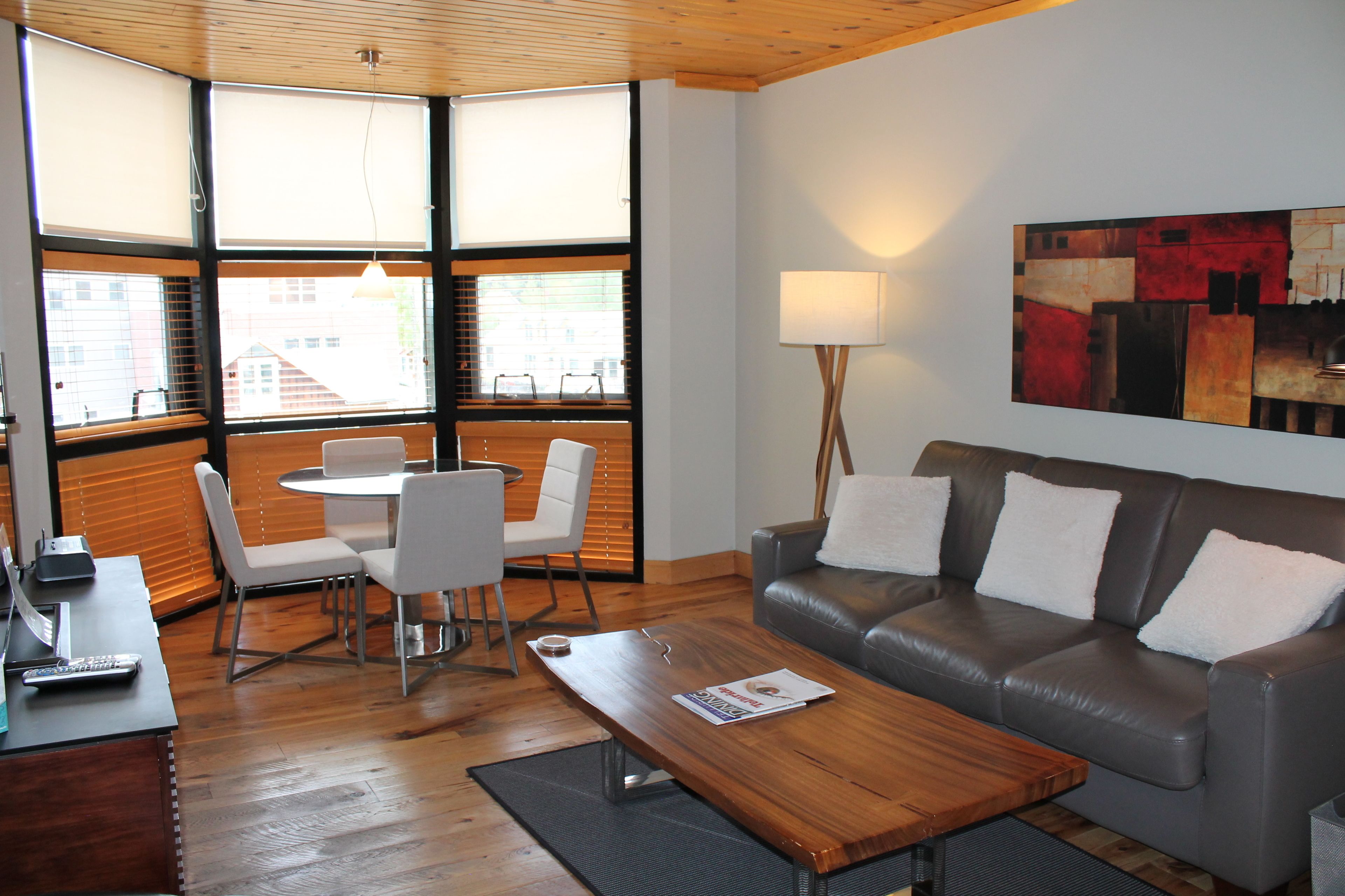 A modern living room with a leather sofa, a wooden coffee table, and a dining area with a white table and chairs.