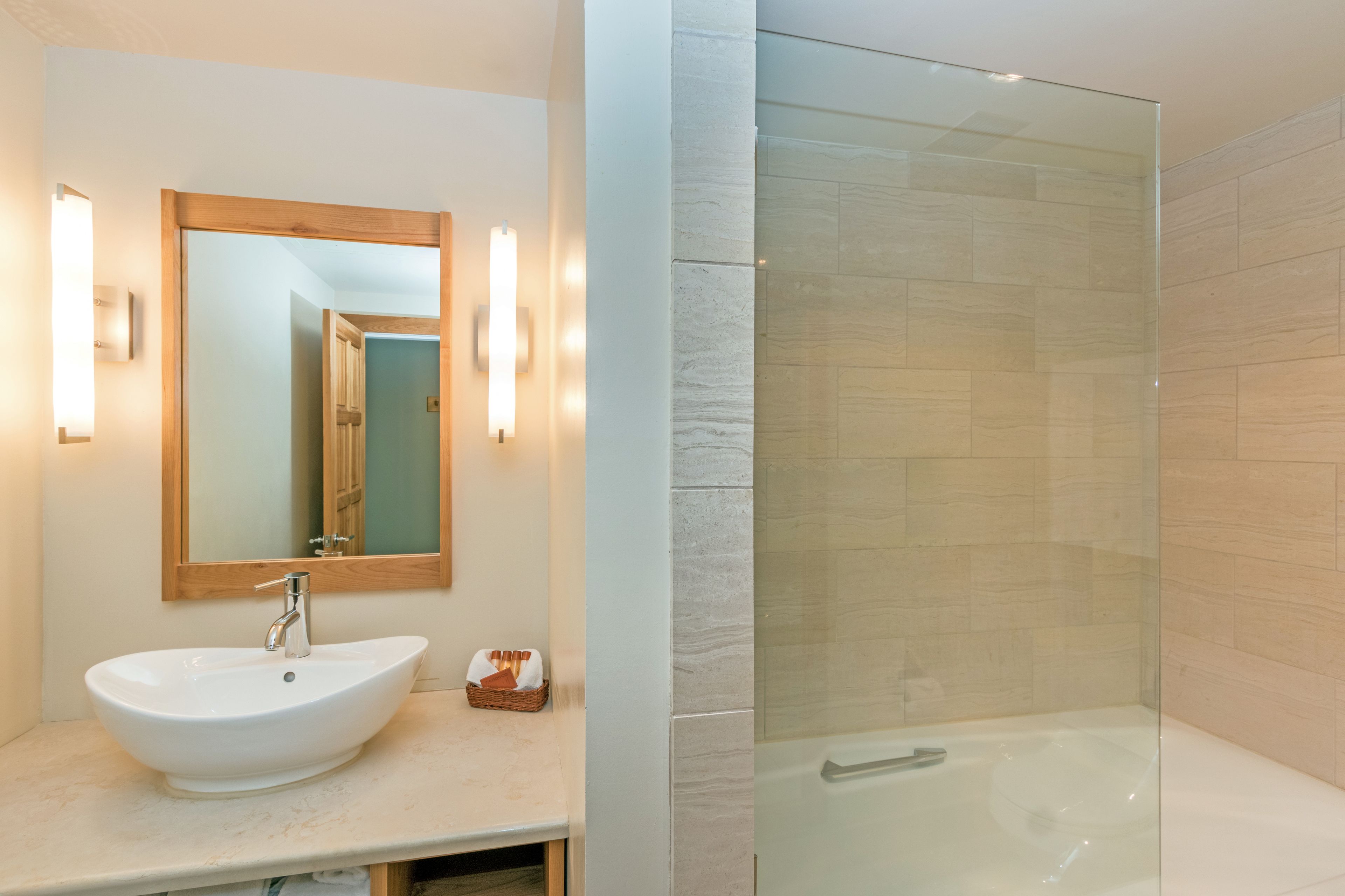 A bathroom with a white sink, a wooden-framed mirror, and a glass-enclosed shower area.