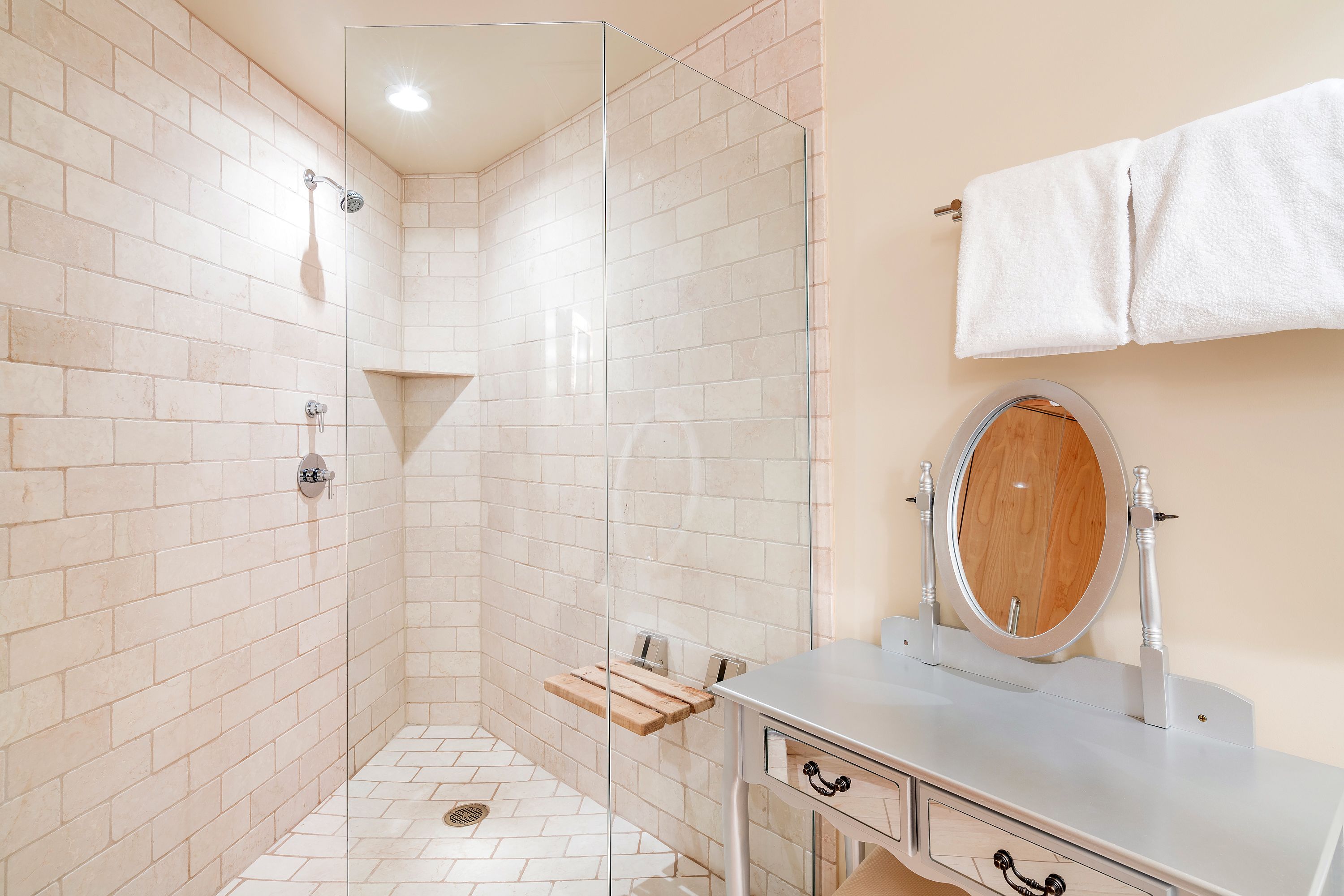 A bathroom with a glass shower enclosure, a wooden shelf, a sink with a mirror, and a towel rack.