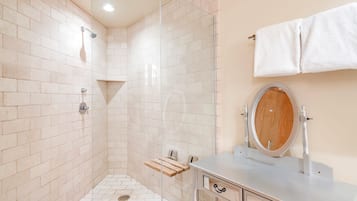 A bathroom with a glass shower enclosure, a wooden shelf, a sink with a mirror, and a towel rack.