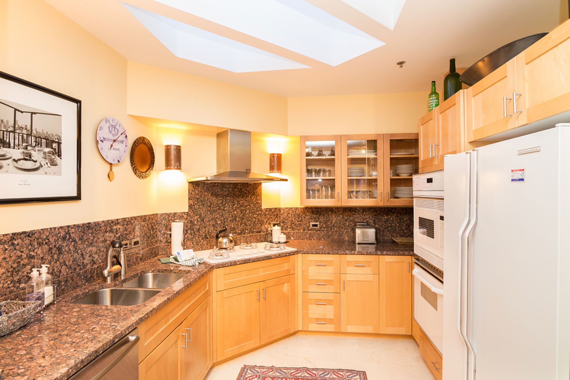 Una cocina con encimeras de granito, gabinetes de madera, un lavamanos de acero inoxidable, horno empotrado y refrigerador.