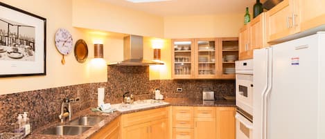 A kitchen with granite countertops, wooden cabinets, a stainless steel sink, a built-in oven, and a refrigerator.
