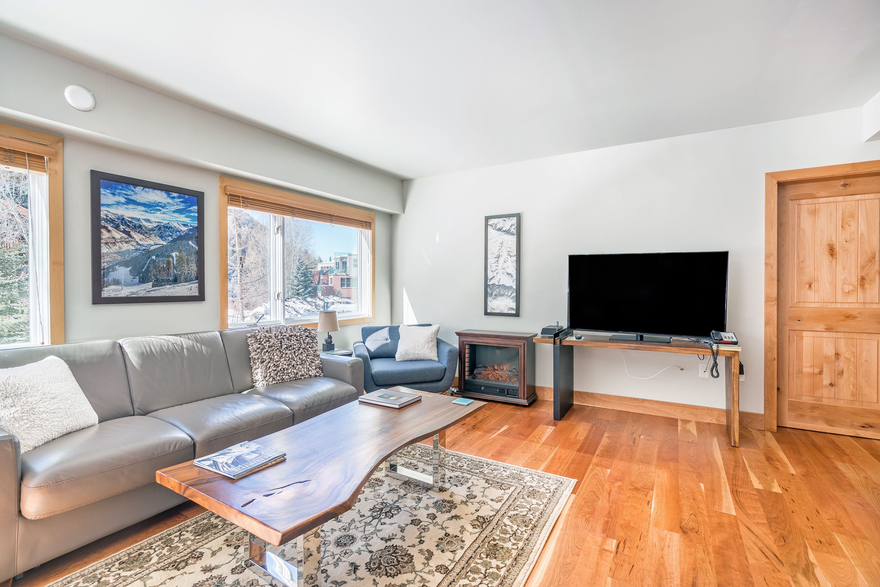 A modern living room with a sofa, coffee table, TV, fireplace, and large windows.