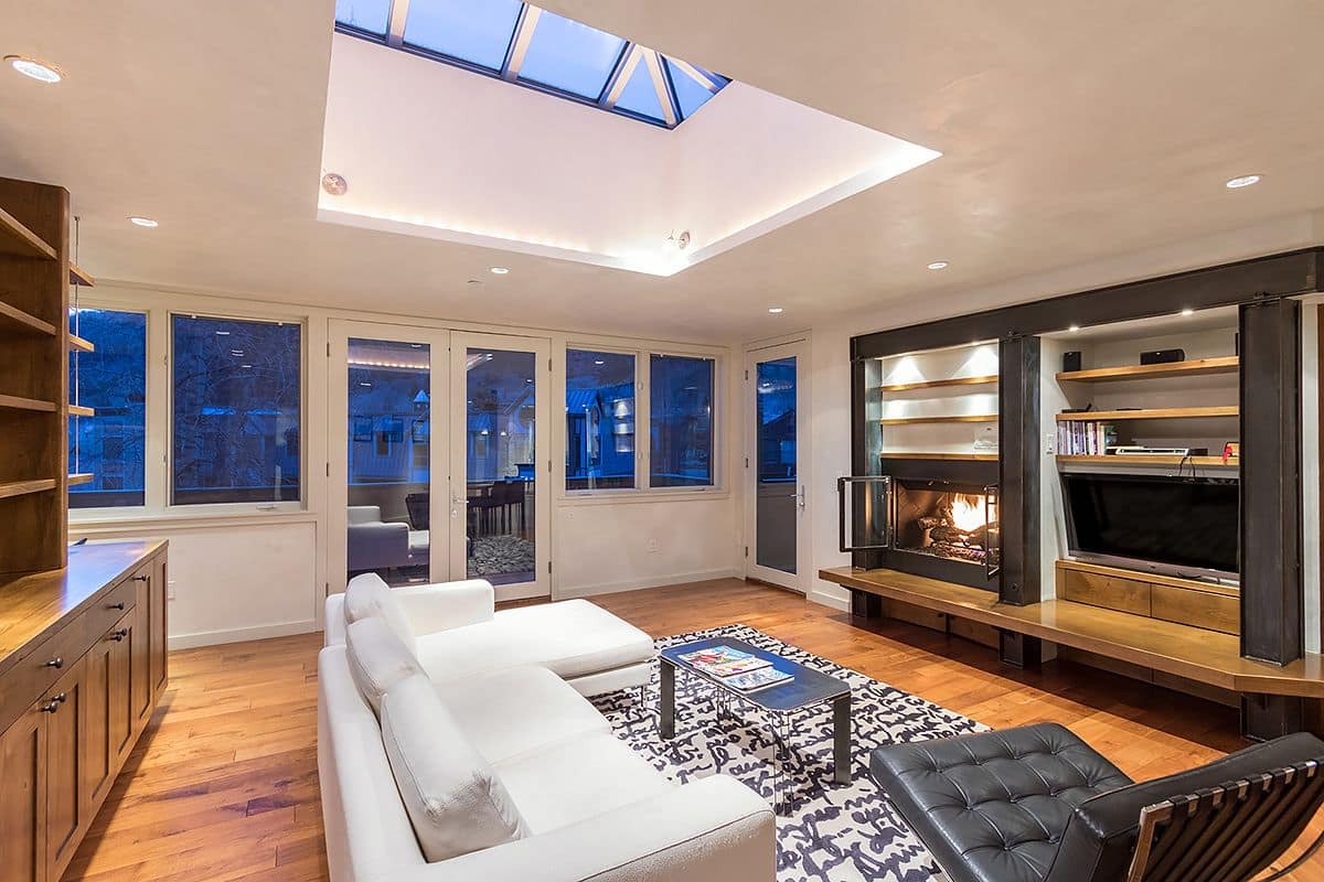 Una sala de estar moderna con tragaluces, ventanas amplias, chimenea y estanterías empotradas.