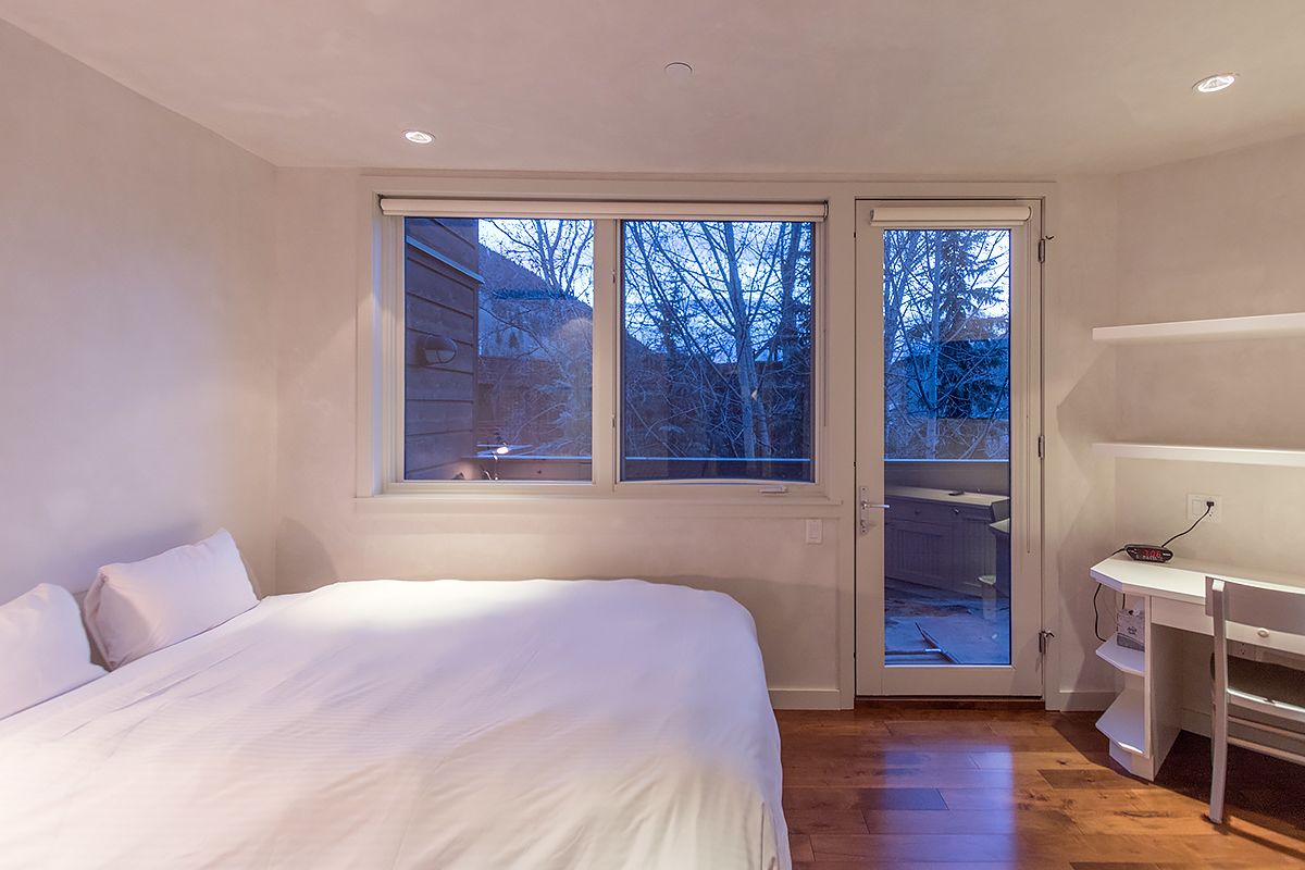 A bedroom with a bed, a desk, and a sliding glass door leading to an outdoor area.