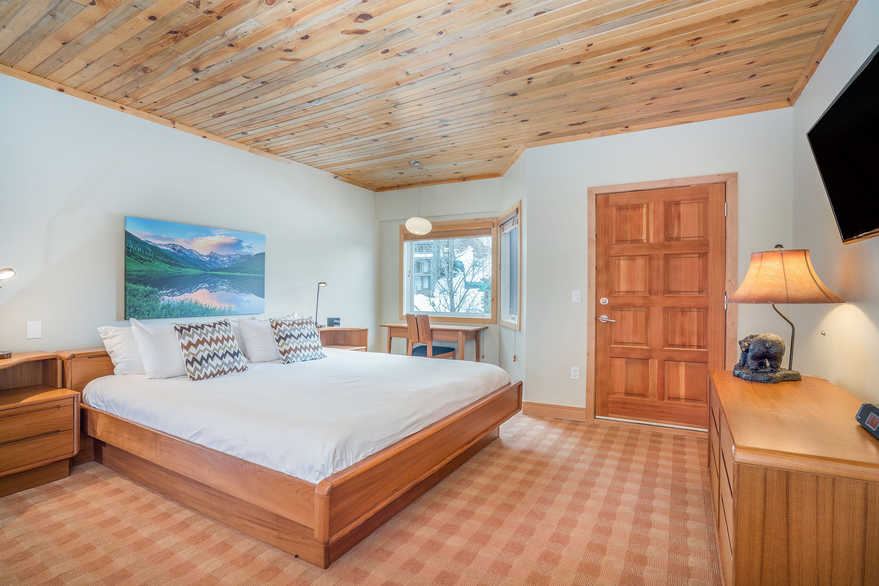 Une chambre à coucher avec un lit en bois, un bureau, une chaise, un téléviseur et une porte.