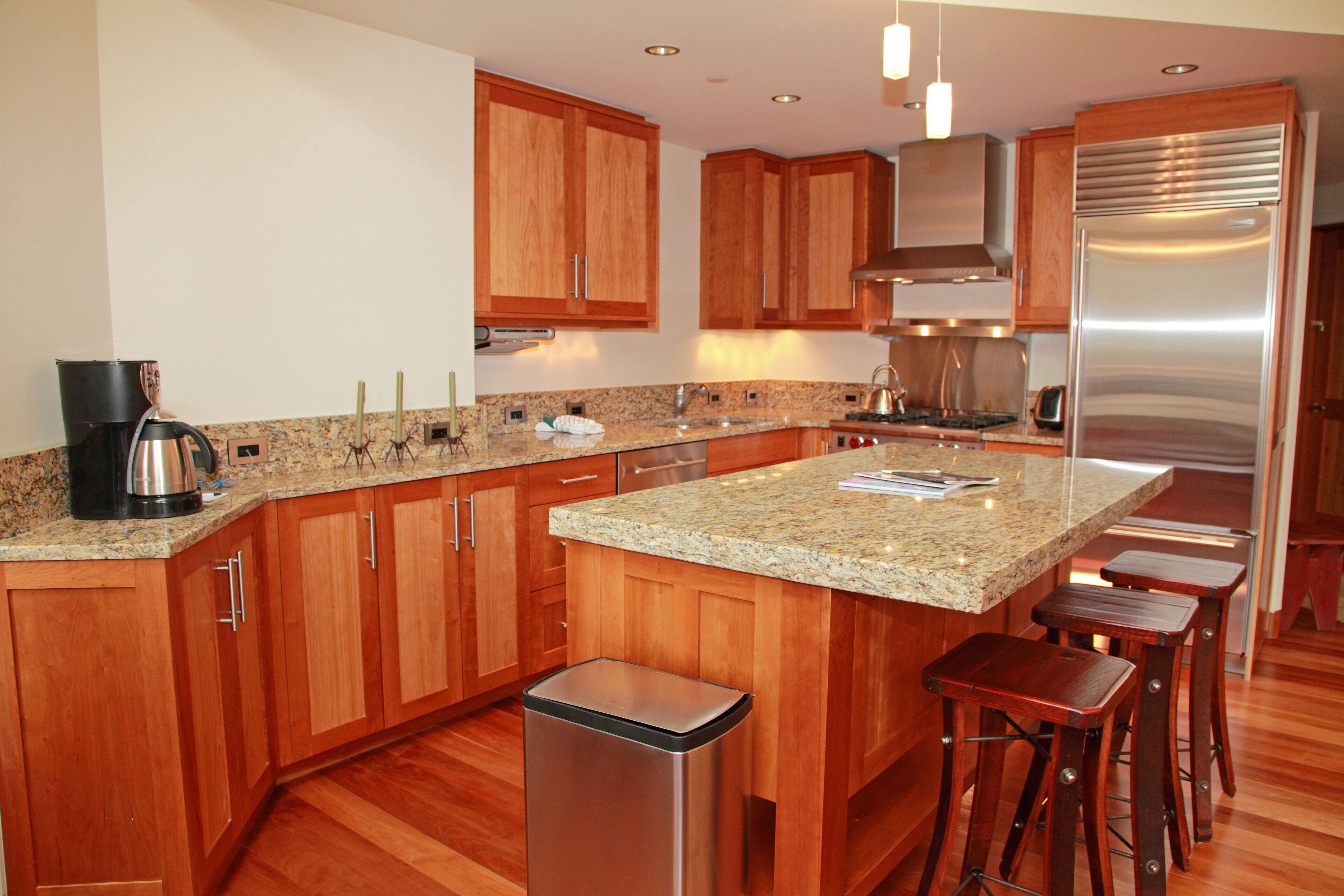 Eine moderne Küche mit Holzschränken, Granit-Arbeitsplatten, Edelstahlgeräten und Barhocker.