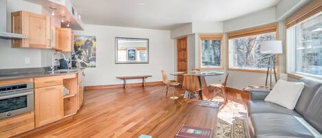 A modern kitchen with wooden cabinets, a dining area with a table and chairs, and a cozy living room with a sofa and a lamp.
