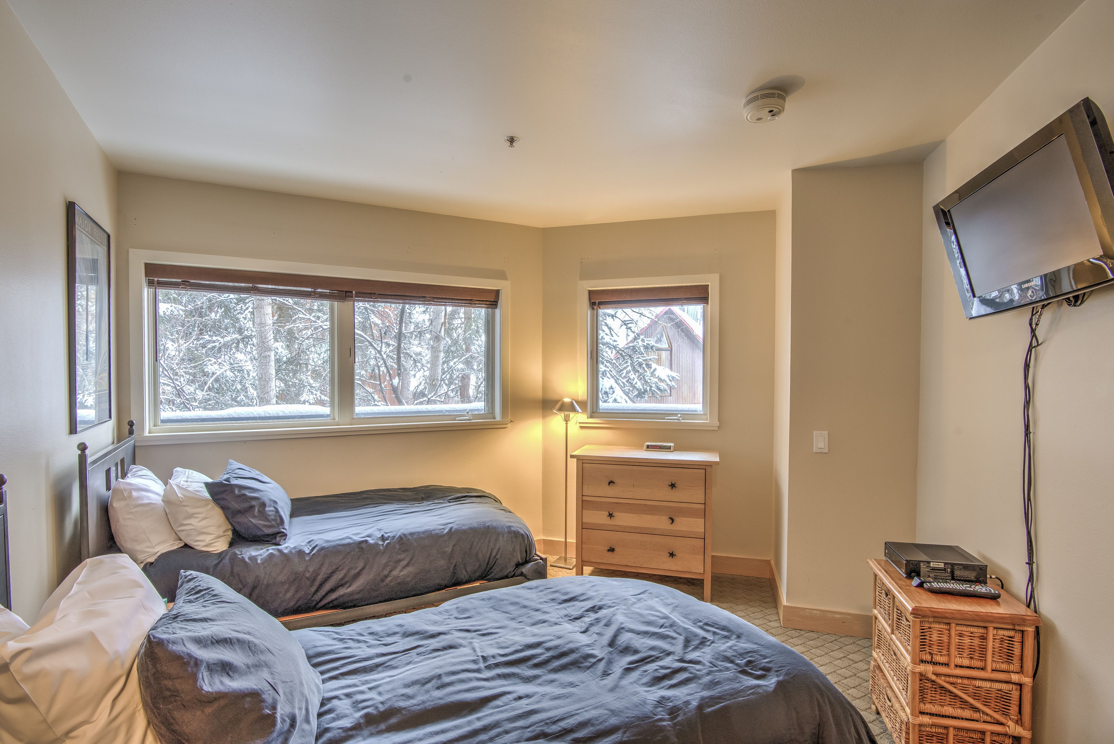 A bedroom with two beds, a nightstand, a dresser, a TV, and large windows.