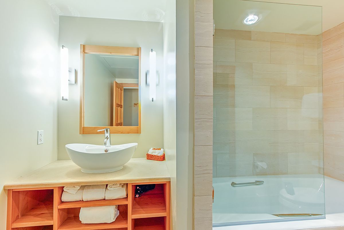 A modern bathroom with a large white sink, a wooden vanity, a glass shower enclosure, and a mirror above the sink.