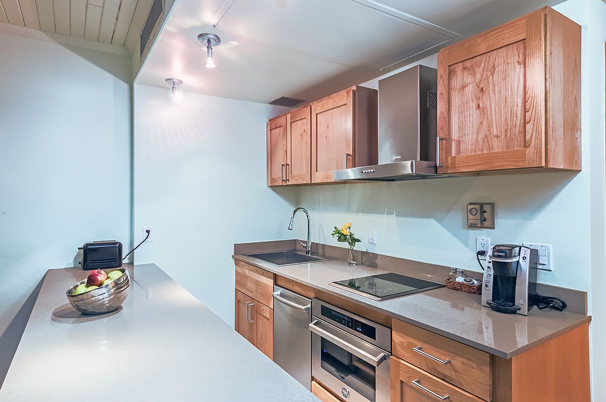 A modern kitchen with wooden cabinets, stainless steel appliances, and a bowl of fruit on the counter.