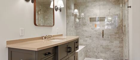 A modern bathroom with a beige vanity, a large mirror, and a glass-enclosed shower area.