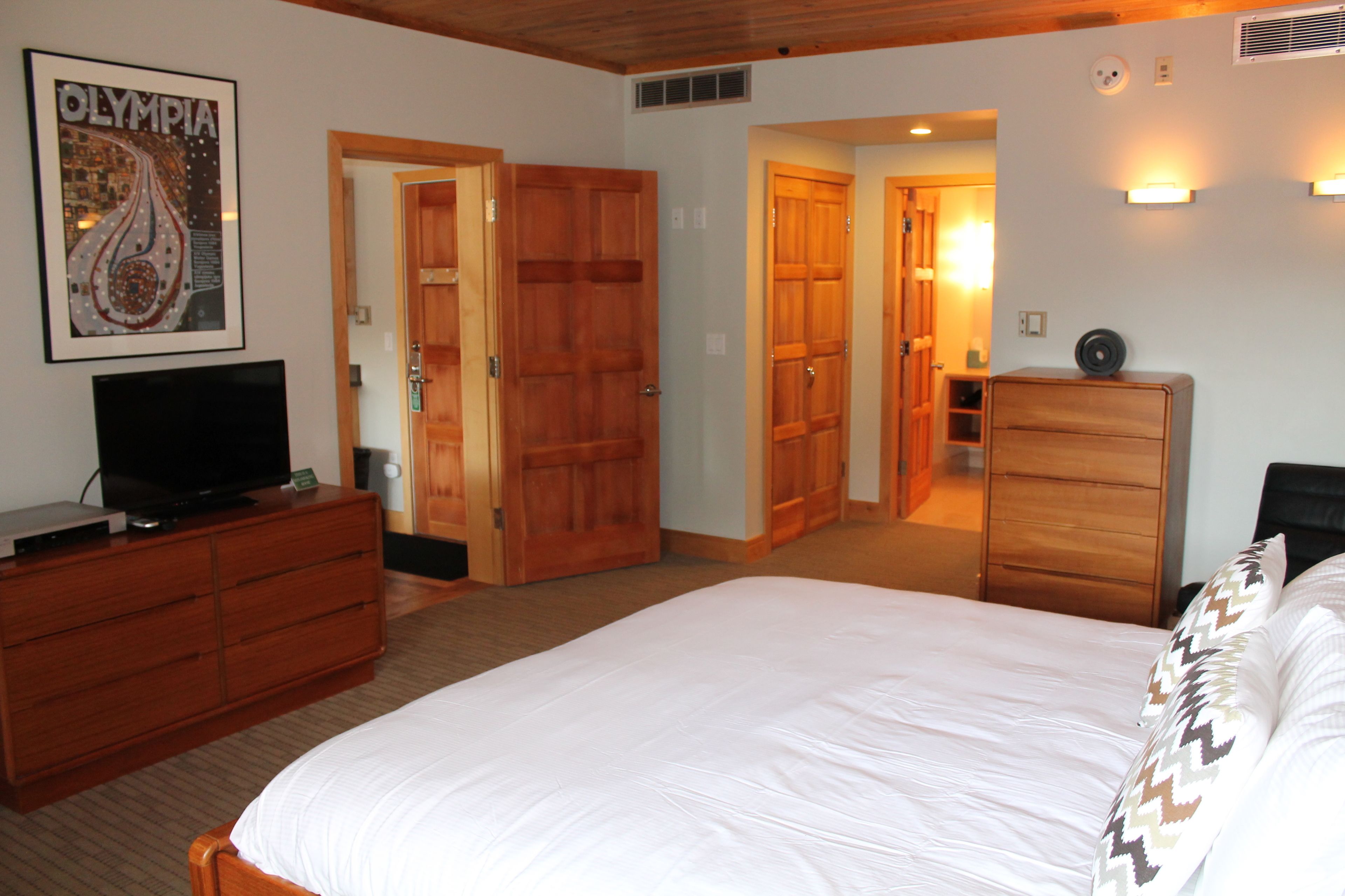 Une chambre d’hôtel avec un grand lit, une armoire en bois, un téléviseur posé sur une commode et un tableau encadré au mur.