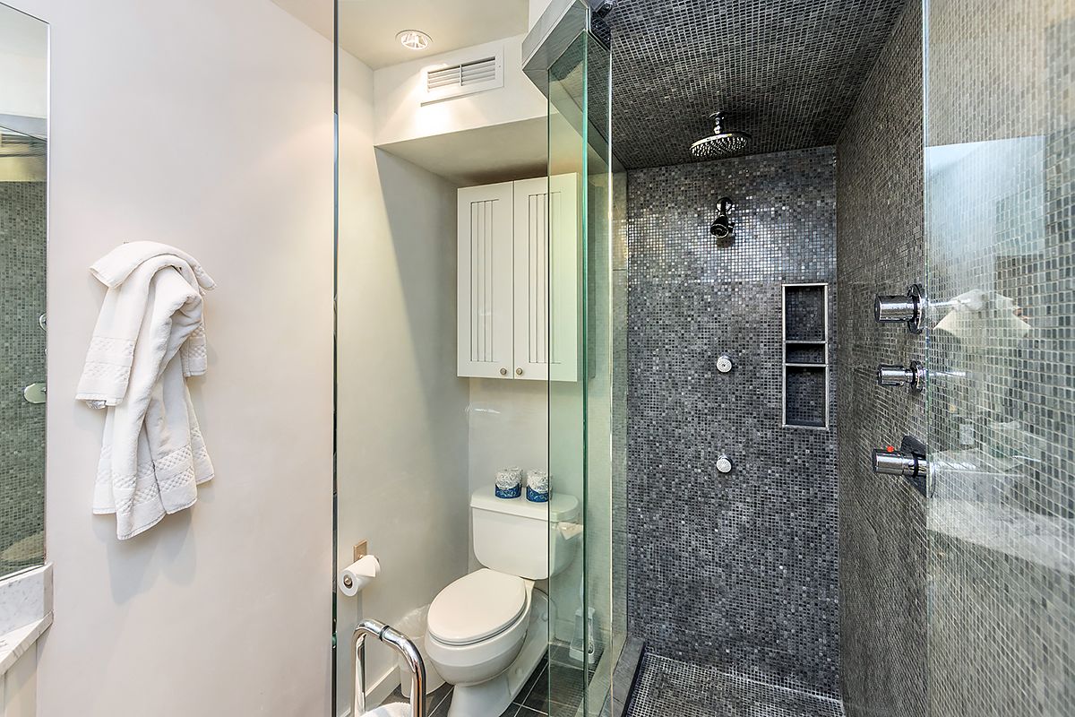 Un baño moderno con ducha envuelta en vidrio, inodoro blanco y un mueble blanco.