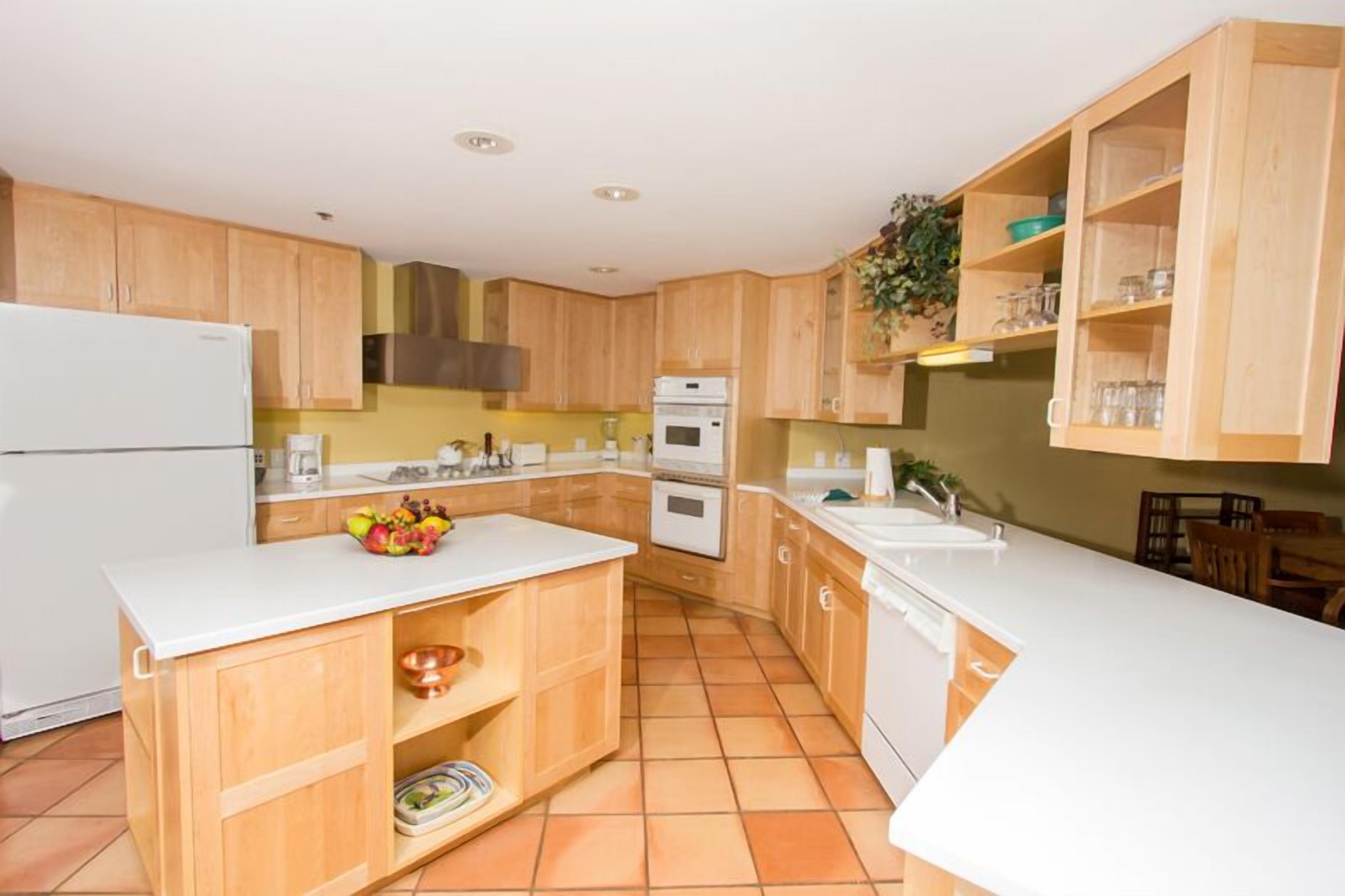 Una cocina compacta con armarios de madera, una encimera blanca y suelo de baldosas.