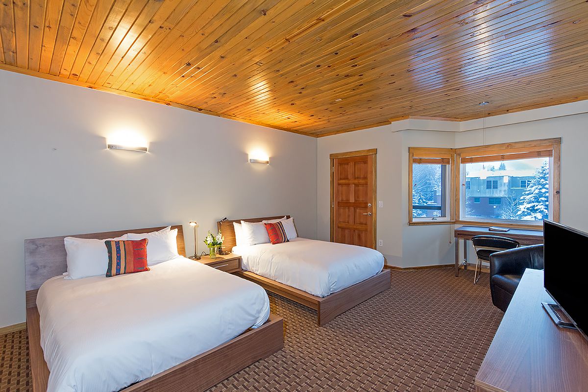 A hotel room with two beds, a desk, a chair, and a TV.