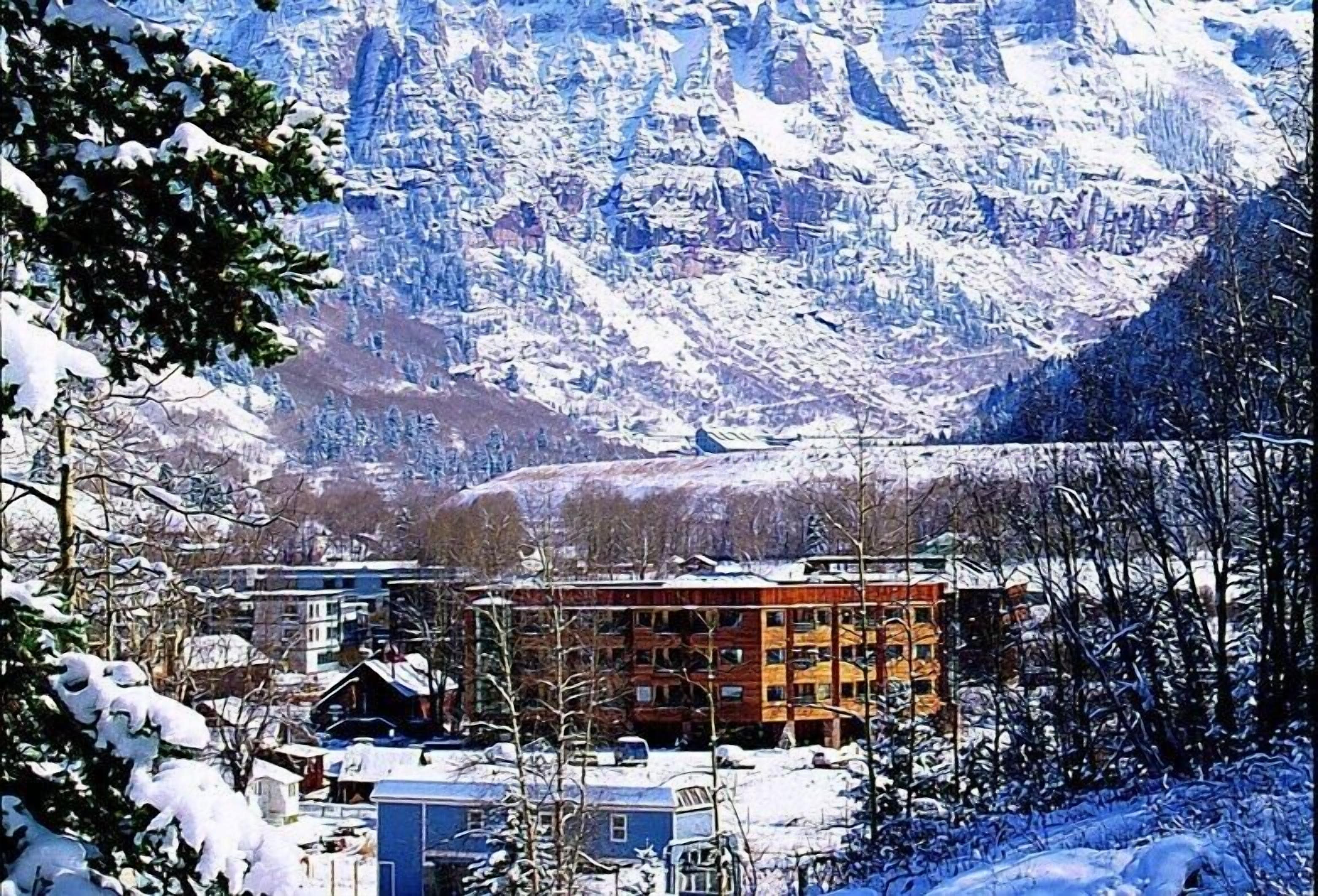 Paisagem montanhosa coberta de neve, com um edifício de vários andares em primeiro plano.