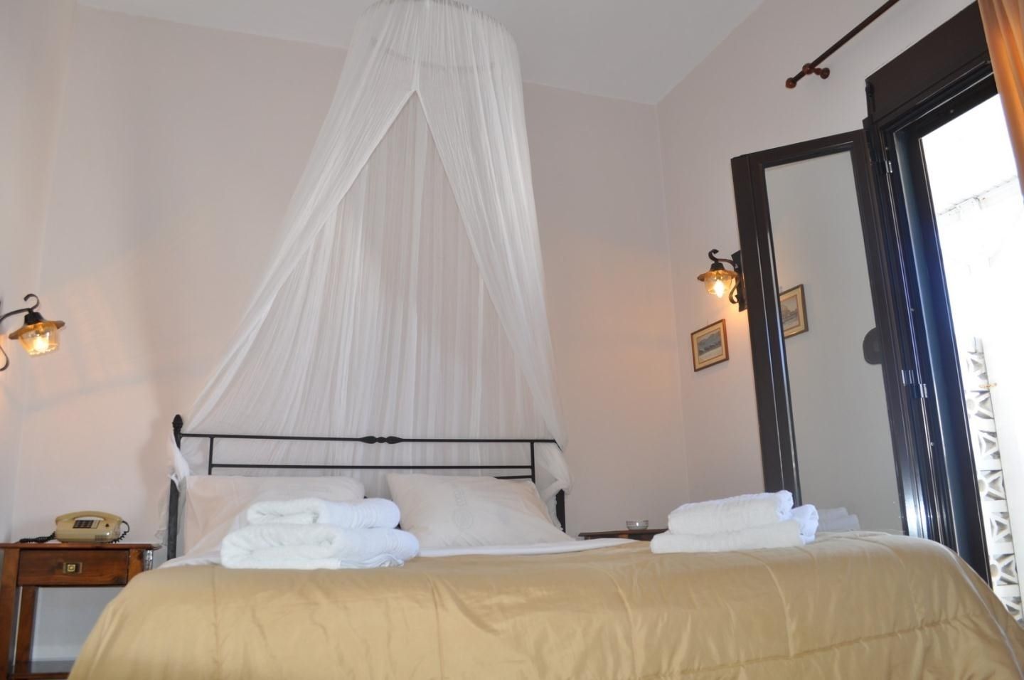 A bedroom with a canopy bed, bedside lamps, a bedside telephone, and a view of the outside through a door.