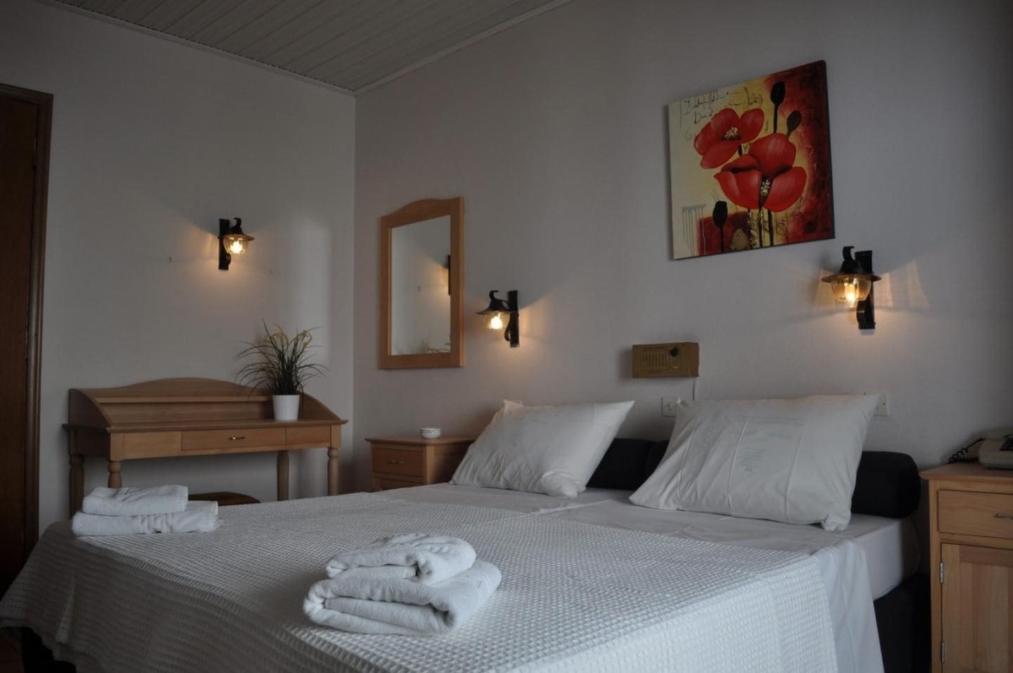 Ein Hotelzimmer mit einem Bett, Nachttischen, einer Holzkommode, einem Spiegel und Wandleuchten.