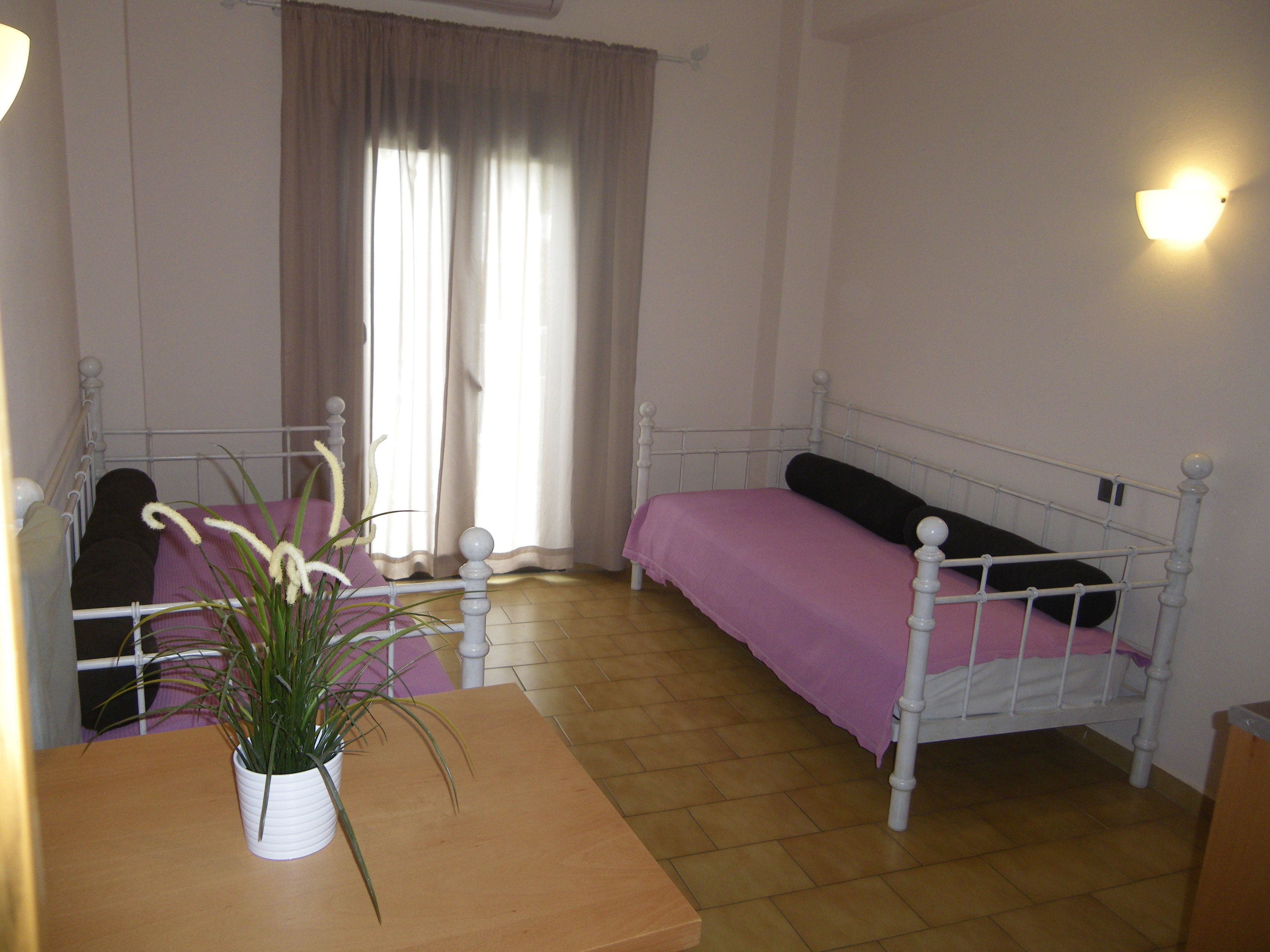 A bedroom with a bed, a bedside table, a potted plant, and a window with curtains.