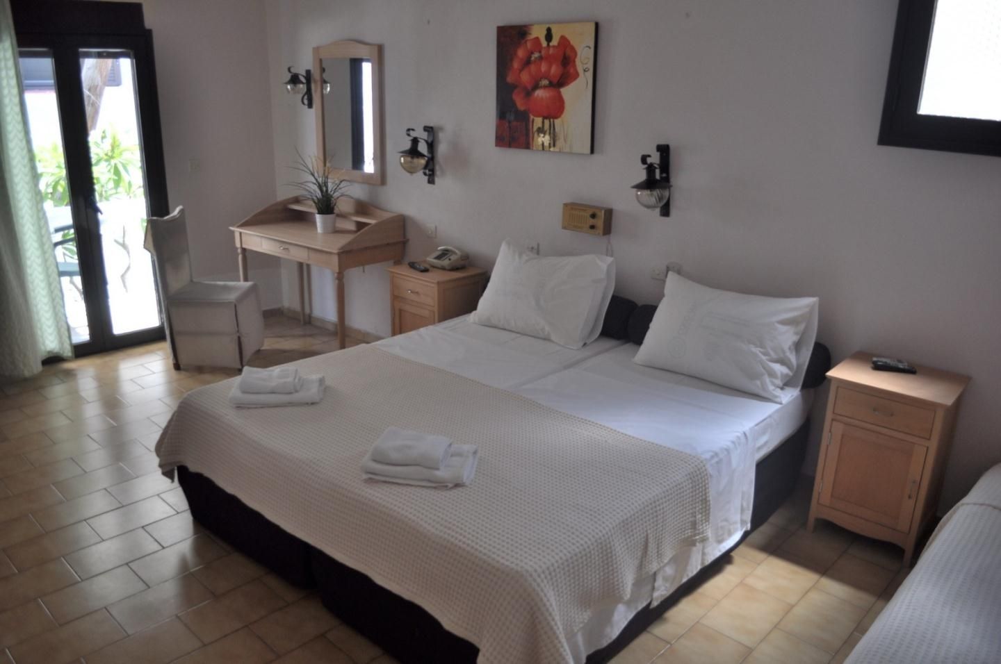 A hotel room with a large bed, a desk, a chair, a nightstand, and a painting on the wall.