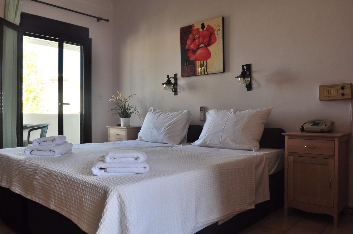 Una habitación de hotel con una cama, una mesita de noche con lámpara, un teléfono en la pared y un cuadro.