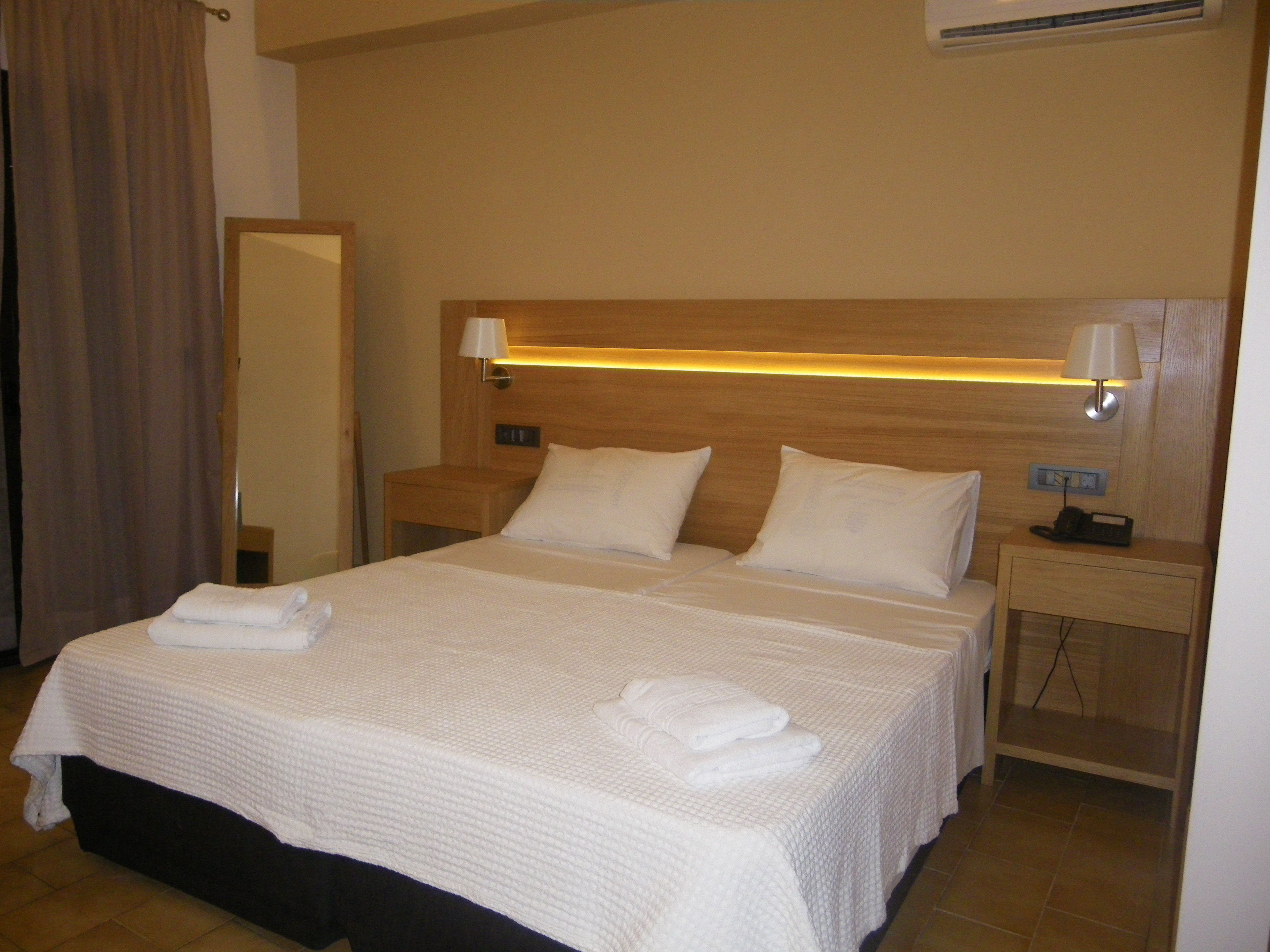 Ett hotellrum med en stor säng, två sängbord, ett litet bord, en lampa och en spegel.