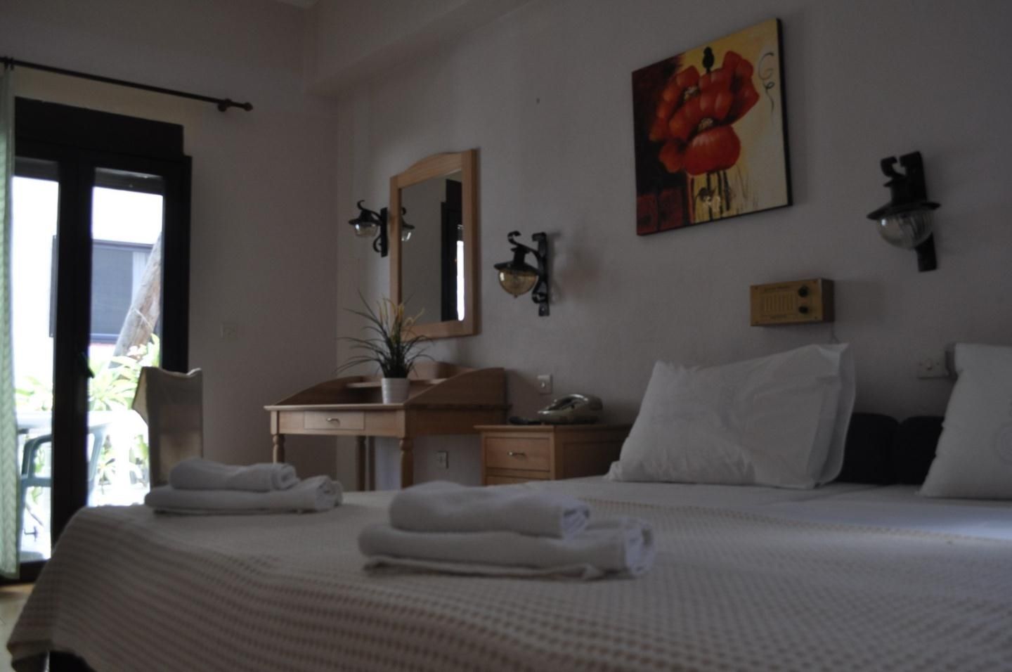 A hotel room with a bed, a desk, a chair, a mirror, a painting, and a window.