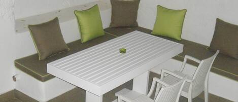 Een witte tafel met een bank en witte stoelen, met groene kussens.