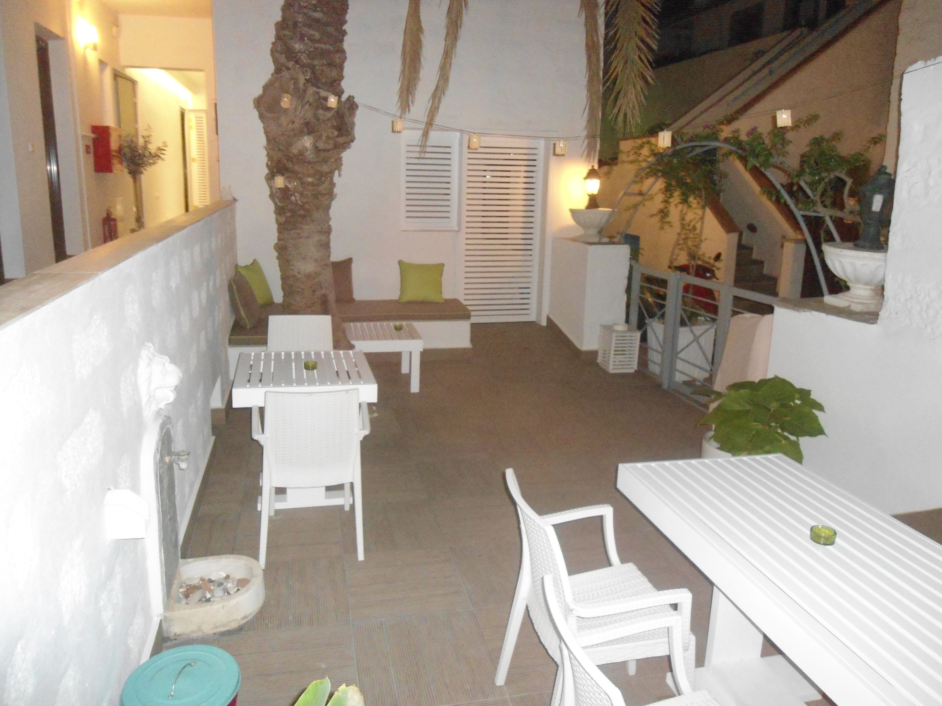Un patio con mobiliario blanco, que incluye una mesa y sillas, un rincón de estar pequeño con cojines y una palmera.